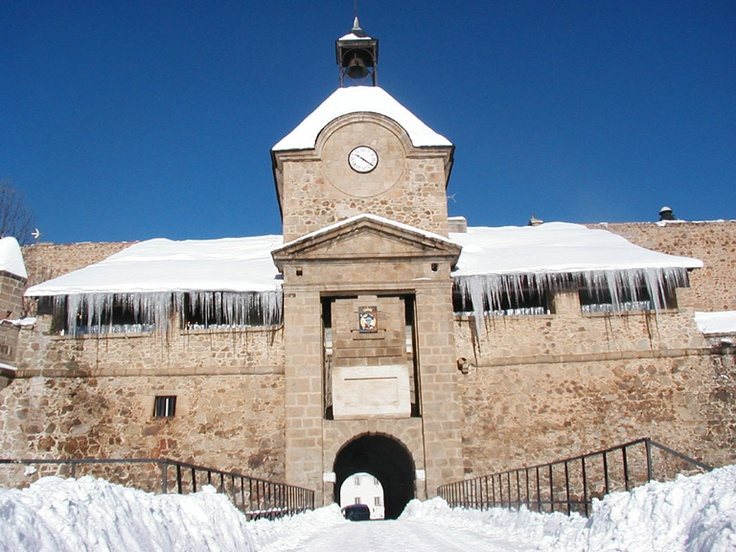 Porte d'entrée de la citadelle de Mont-Louis sous la neige, toits enneigés et stalactites de glace.